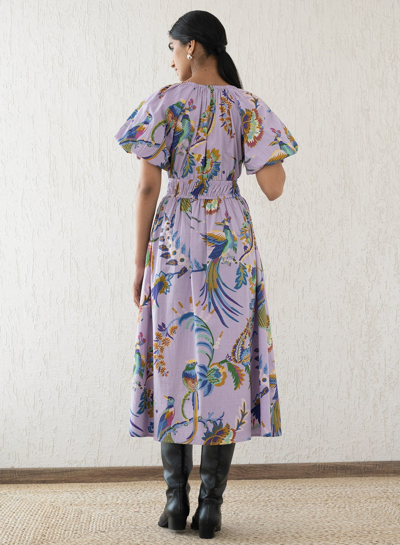 Back view of a woman wearing the Francesca dress in Vienna Waltz Lilac print, featuring a flattering V-neck, puffed sleeves, elastic under the bust, and side pockets.