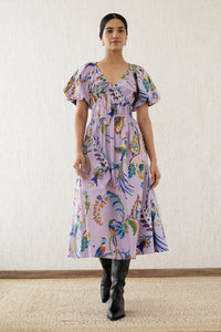 Woman stepping forward wearing the Francesca dress in Vienna Waltz Lilac print, featuring a flattering V-neck, puffed sleeves, elastic under the bust, and side pockets.