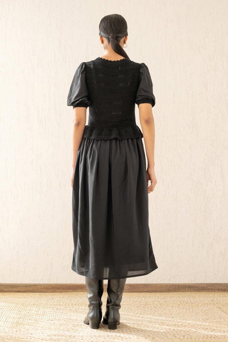 Back view of a woman wearing the Heather maxi dress in black, featuring hand-crocheted details, a woven viscose georgette skirt, and a soft peplum waist for a flattering silhouette.