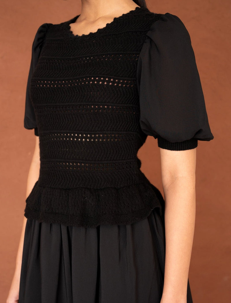 Close up of a woman wearing the Heather maxi dress in black, featuring hand-crocheted details, a woven viscose georgette skirt, and a soft peplum waist for a flattering silhouette.