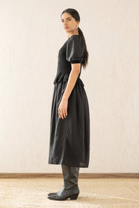 Side view of a woman wearing the Heather maxi dress in black, featuring hand-crocheted details, a woven viscose georgette skirt, and a soft peplum waist for a flattering silhouette.