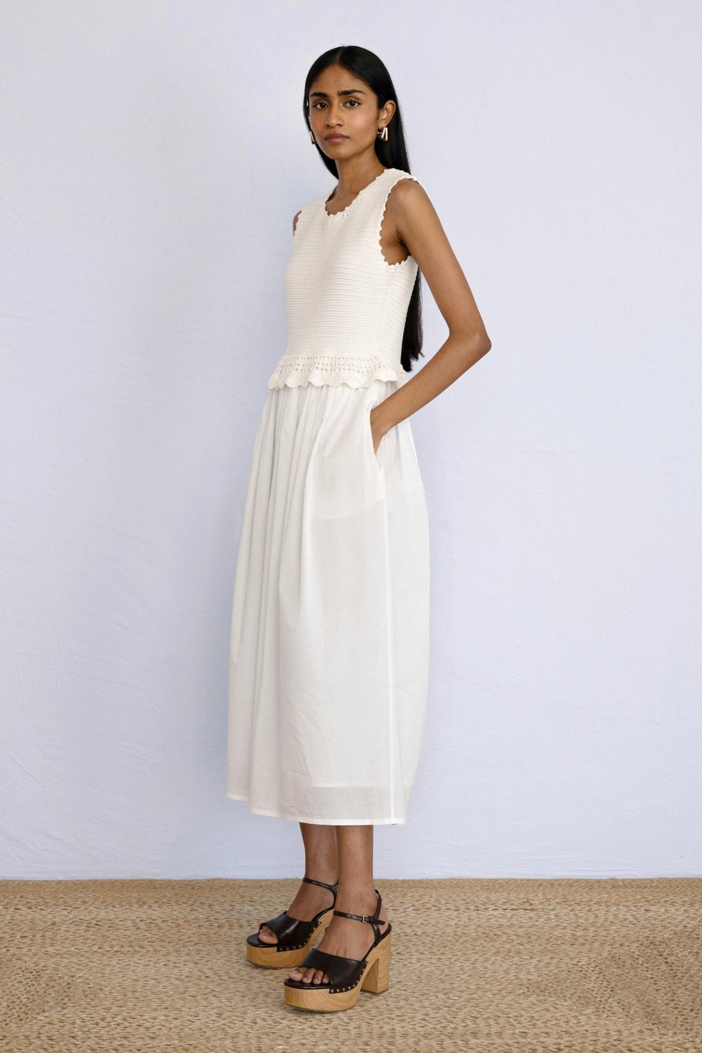 Side view of model standing wearing Heather Crochet Dress in Ivory colour with a hand in pocket.