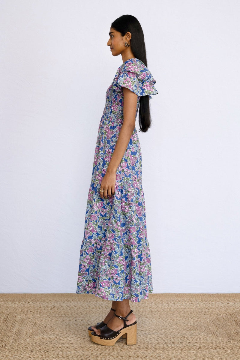 Side view of model standing wearing a full length Ira Dress in Arcadia Dazzling Blue print.