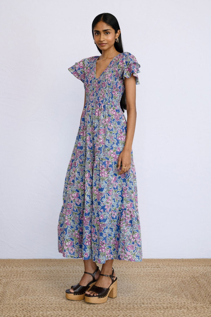 Side view of model posing sideways wearing a full length Ira Dress in Arcadia Dazzling Blue print.