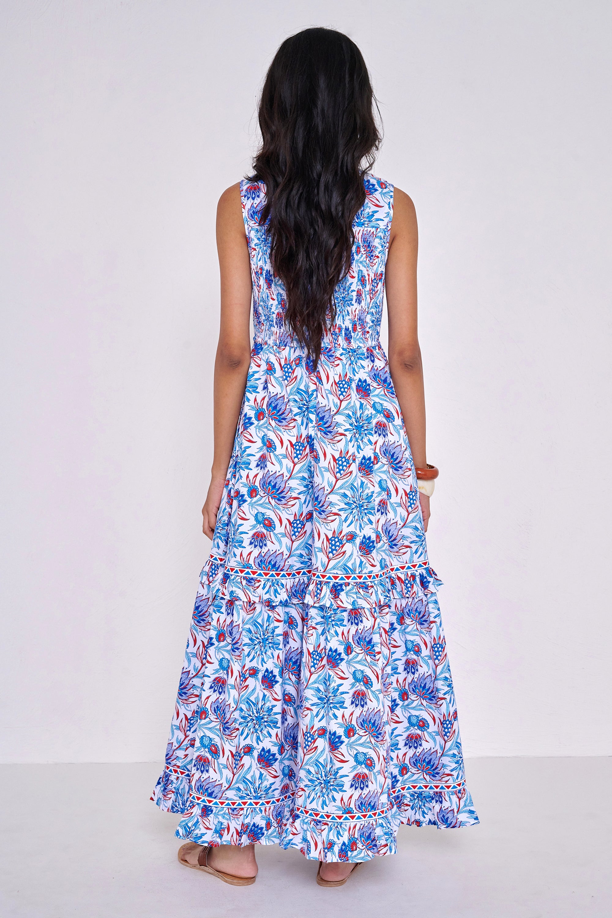 Back view of woman standing. She is  wearing the Iris dress in the Philippa print, featuring a smocked bodice, A-line silhouette, and red, white, and blue floral motifs inspired by Provence’s wild thistles and vines.
