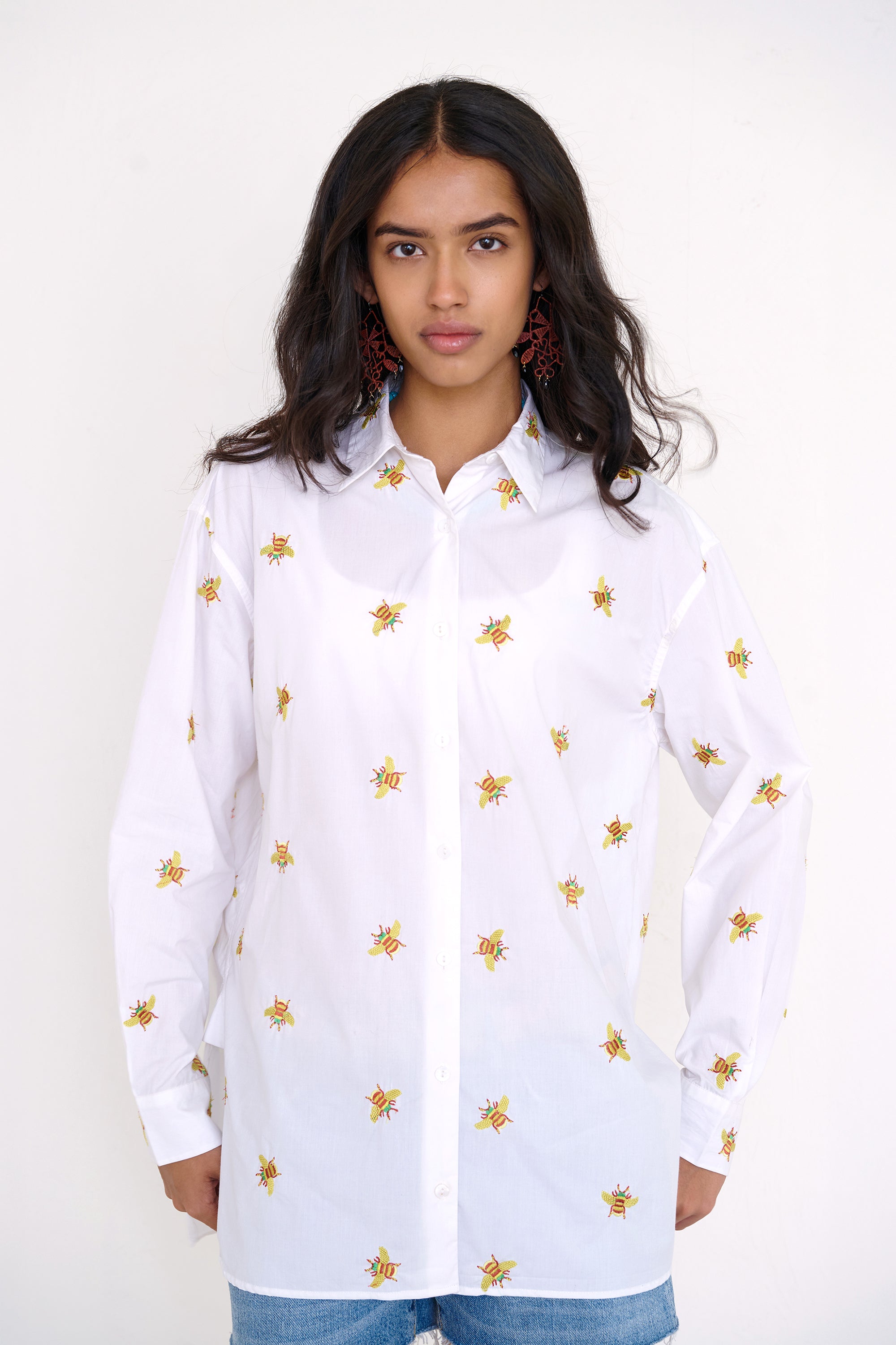 Front view of woman standing wearing the Jamie shirt, featuring a menswear-inspired button-up silhouette, embroidered bumblebee motifs, pleat details, and a high-low hem.
