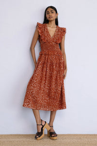 Front view of model posing on wall wearing Keira Dress block printed Bondi Batik print, Tobacco colour.