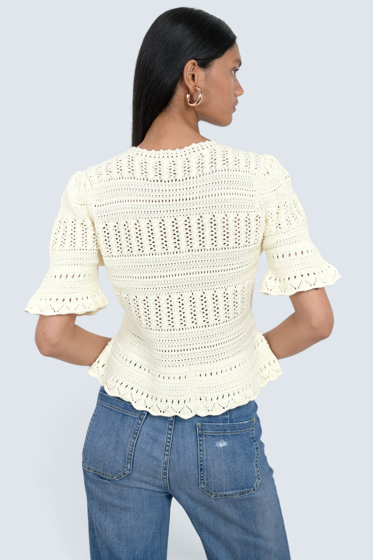 Banjanan ivory cotton short sleeve cardigan with intricate hand-crocheted trim and ruffled sleeves, back view.