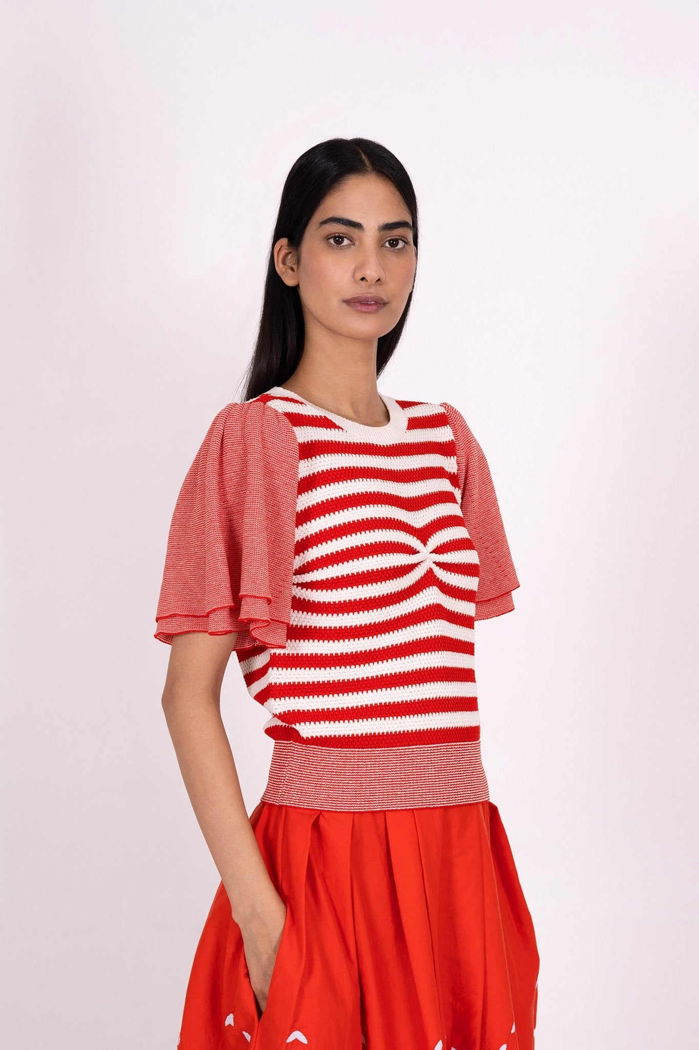 Side view of woman wearing the Leia sweater, featuring engineered stripes and fluttering micro stripe sleeves in a classic red and white pattern for flattering style.