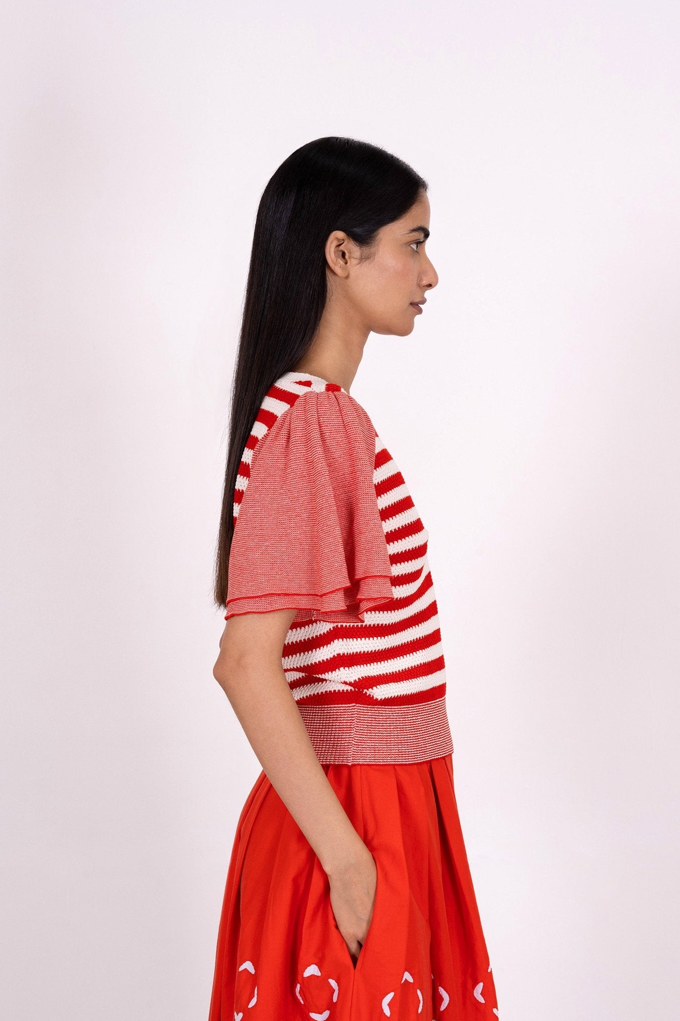 Side view of woman wearing the Leia sweater, featuring engineered stripes and fluttering micro stripe sleeves in a classic red and white pattern for flattering style.