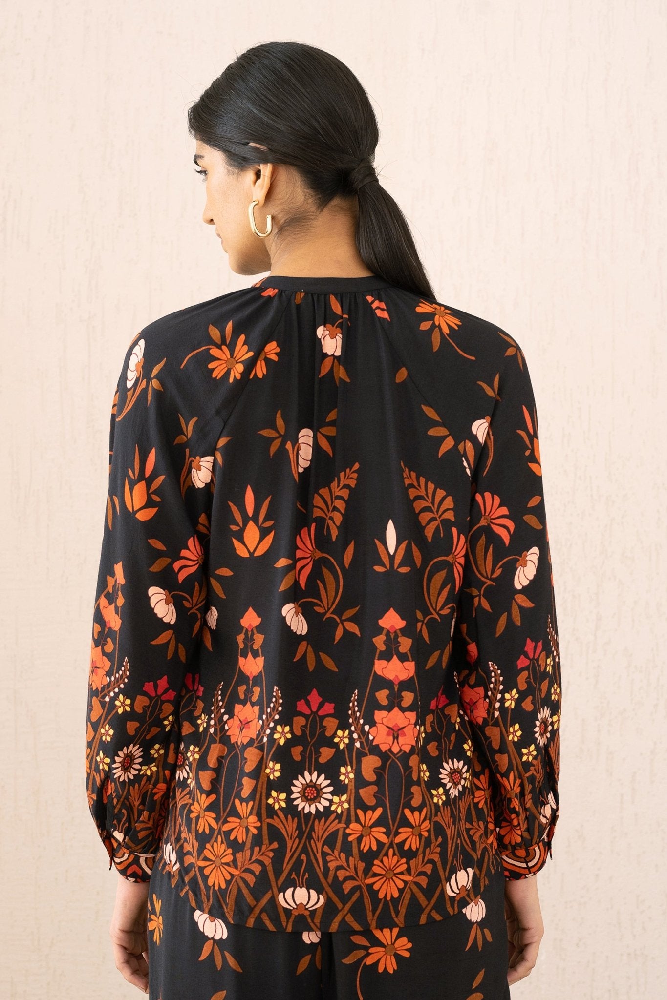 A close-up back view of a woman wearing the Leonie top in Blumen Cedar print, featuring soft gathers at the Mandarin collar and 3/4 raglan sleeves for a flattering drape.