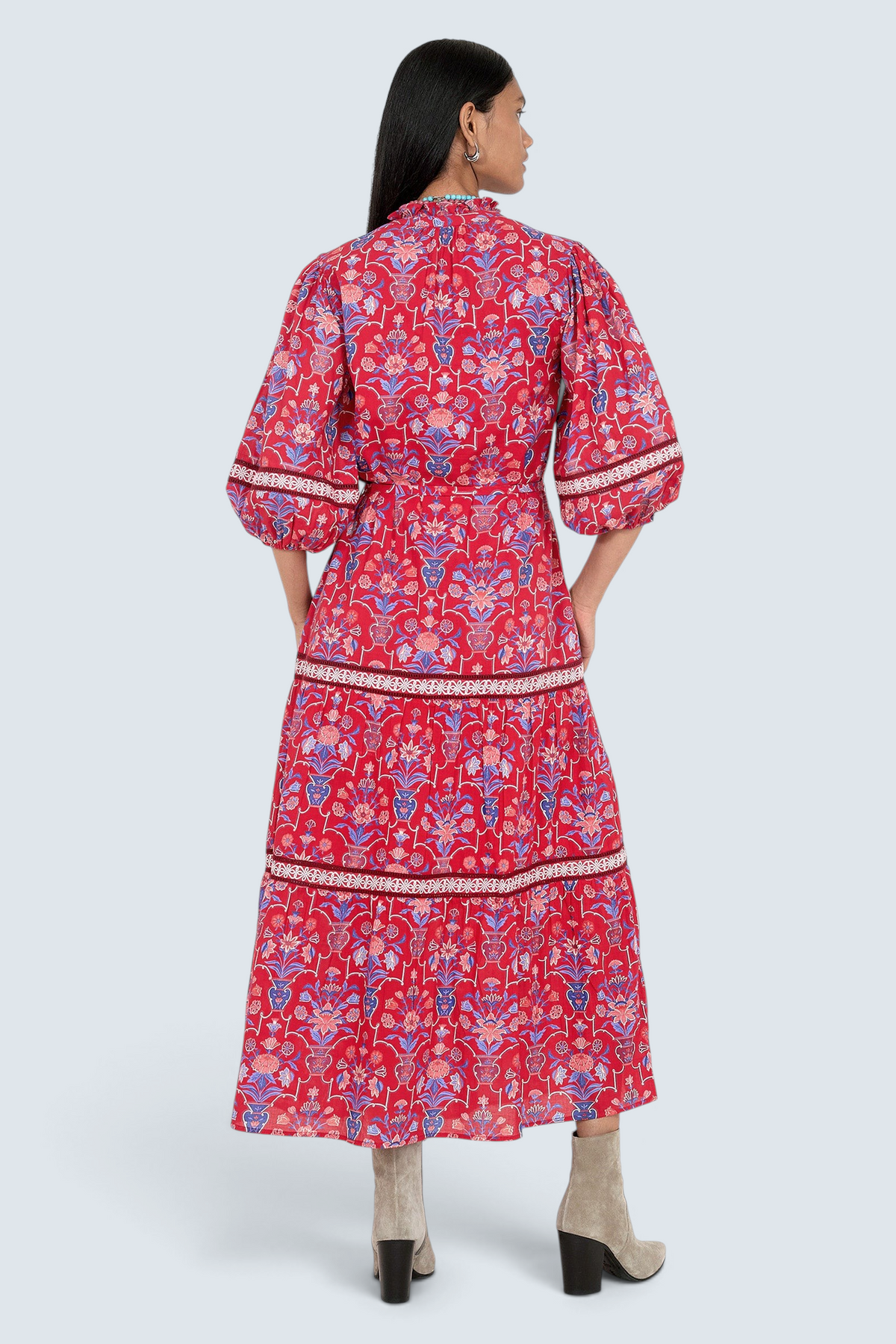 Back view of model standing. She is wearing the Liza dress in Floral Vase print. It features a tie neckline, soft ruffles, lace sleeve and skirt details, and a fabric belt.