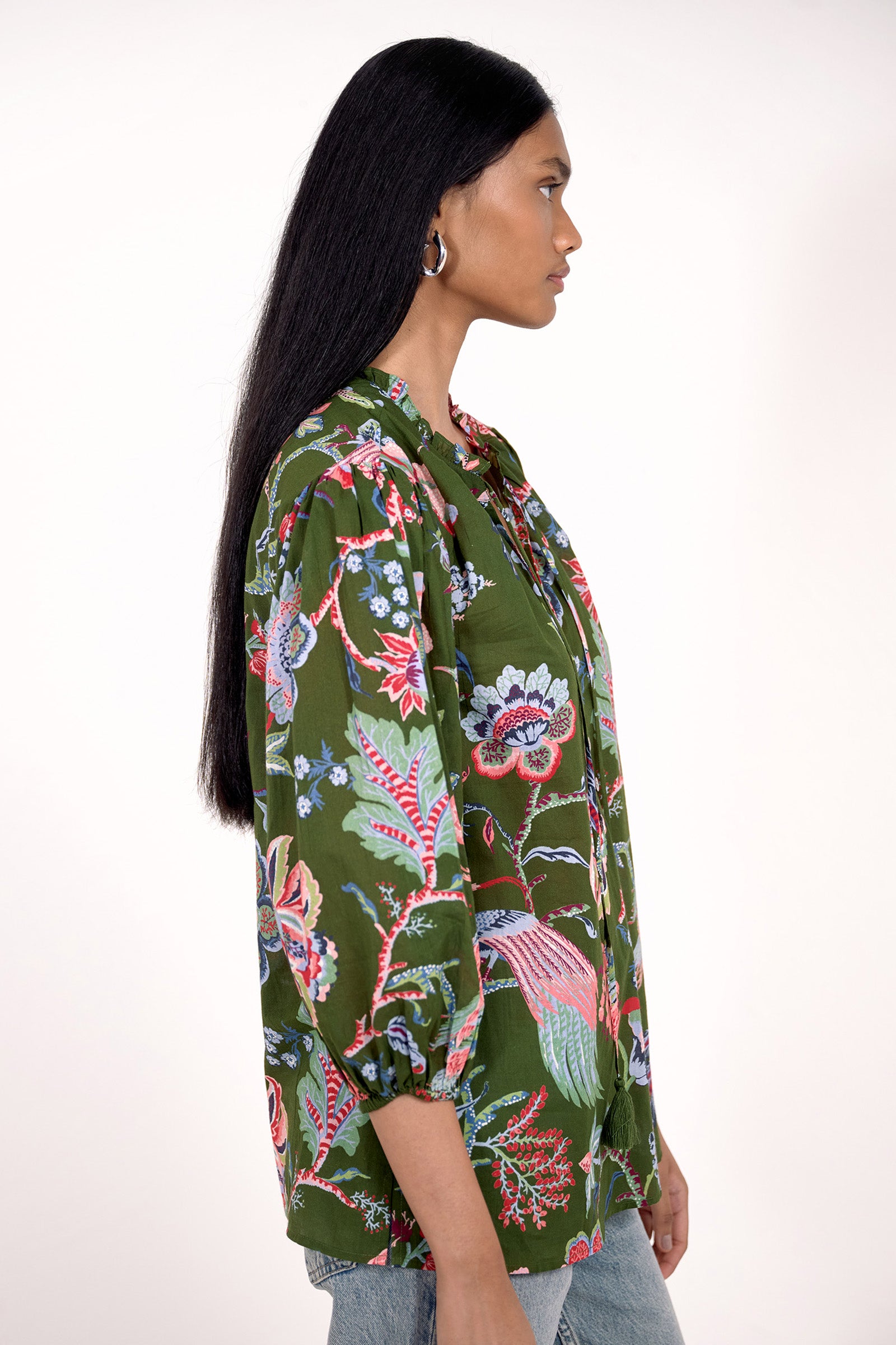 Side view of model standing. She is  wearing the Lorna top in Chintz print, featuring a V-neck with a soft ruffle and tie, a loose flowing body, and slightly voluminous sleeves, paired with jeans.
