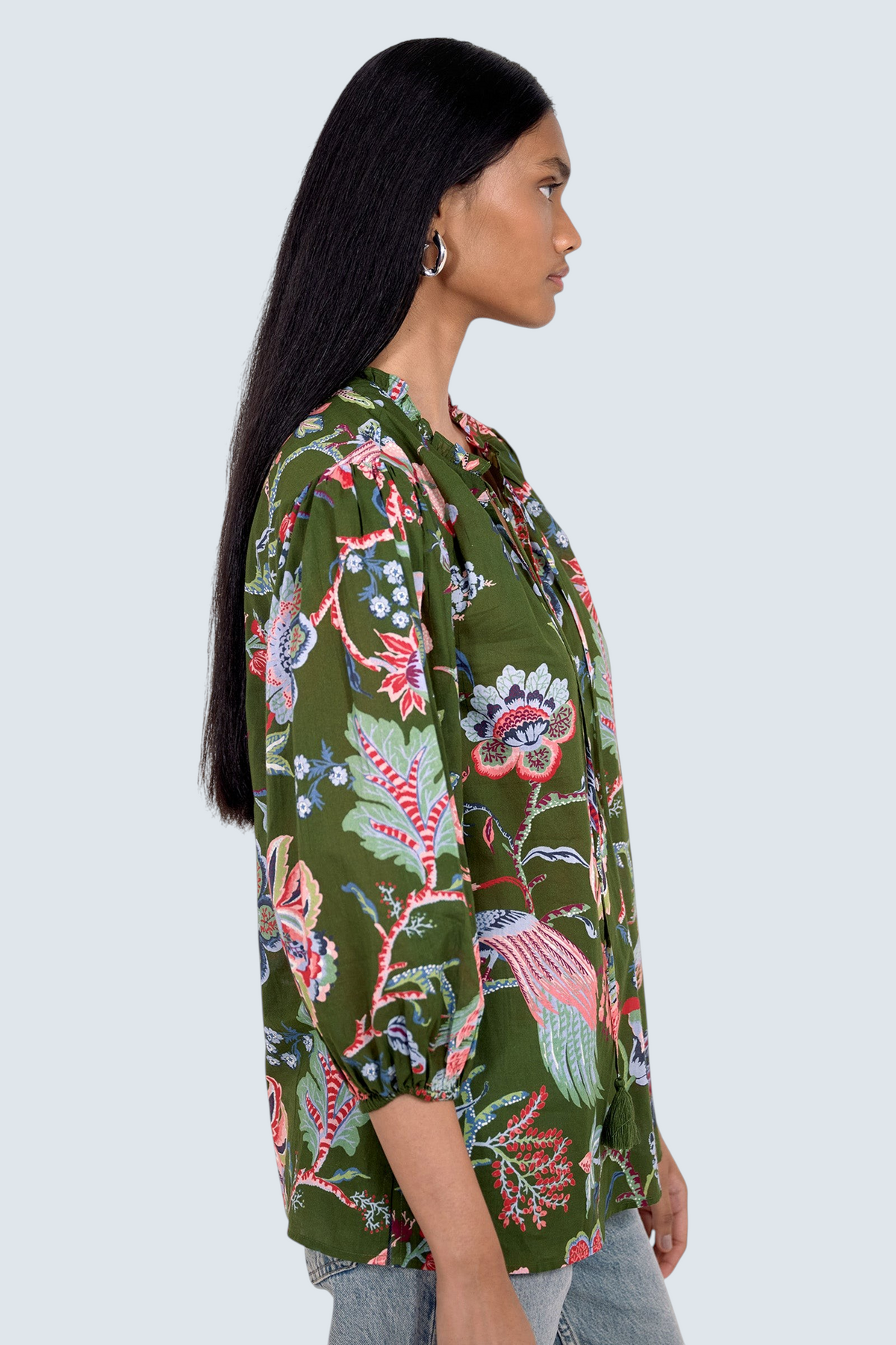 Side view of model standing. She is  wearing the Lorna top in Chintz print, featuring a V-neck with a soft ruffle and tie, a loose flowing body, and slightly voluminous sleeves, paired with jeans.
