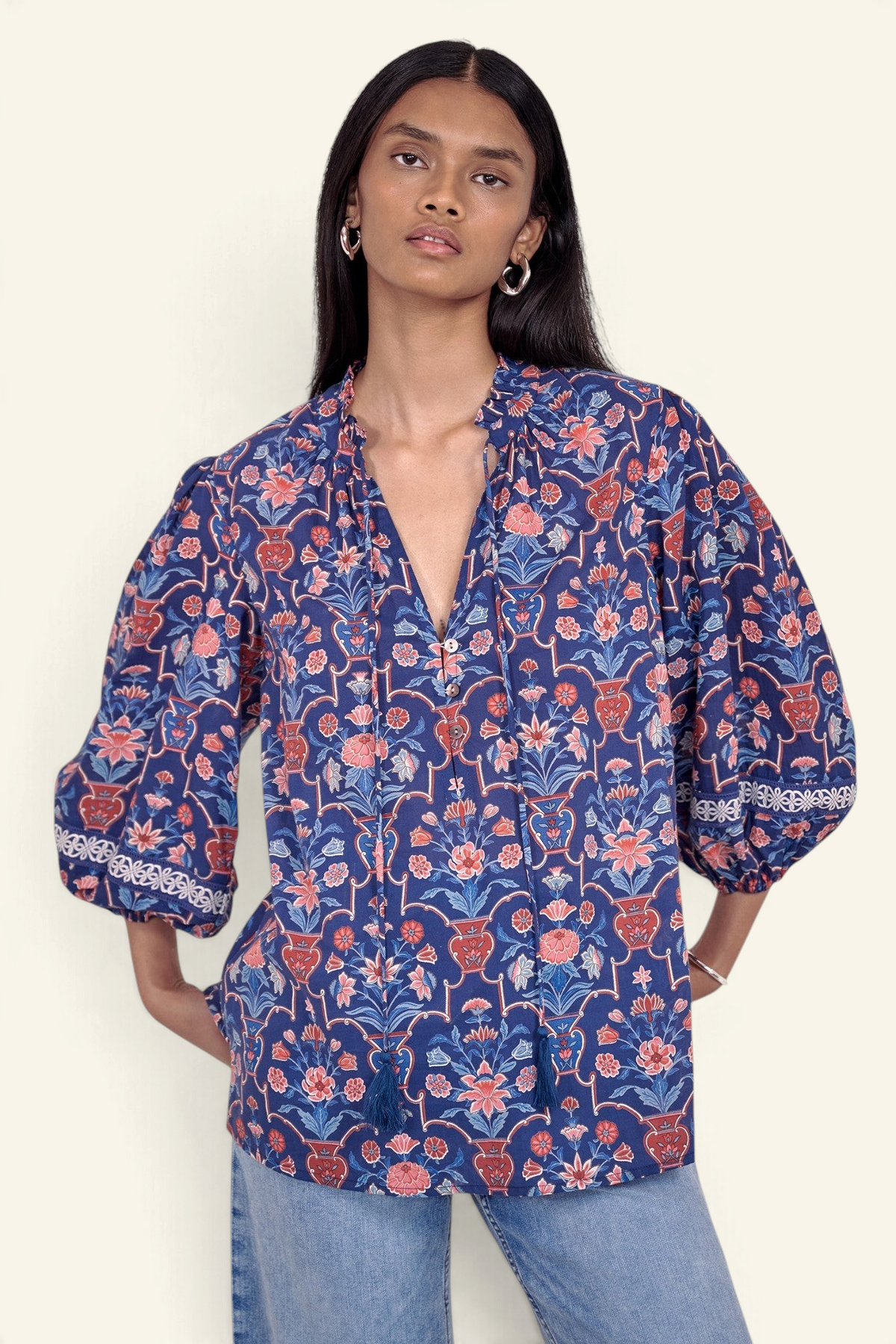 Front view of model standing wearing the Lorna top in Floral Vase print, featuring a V-neck with ruffle and tie, lace-trimmed sleeves, and a loose flowing silhouette, paired with jeans.