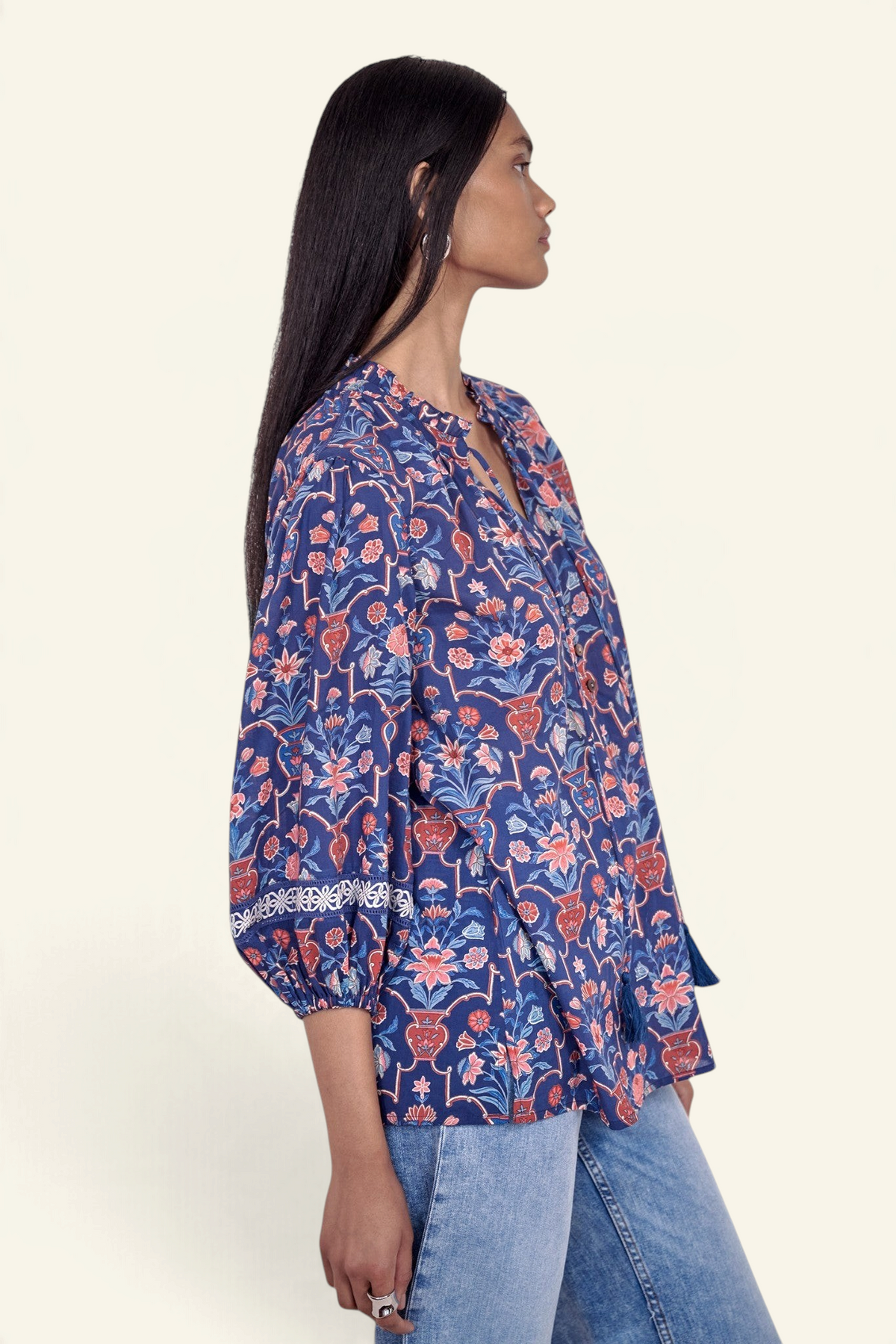 Side view of model standing wearing the Lorna top in Floral Vase print, featuring a V-neck with ruffle and tie, lace-trimmed sleeves, and a loose flowing silhouette, paired with jeans.