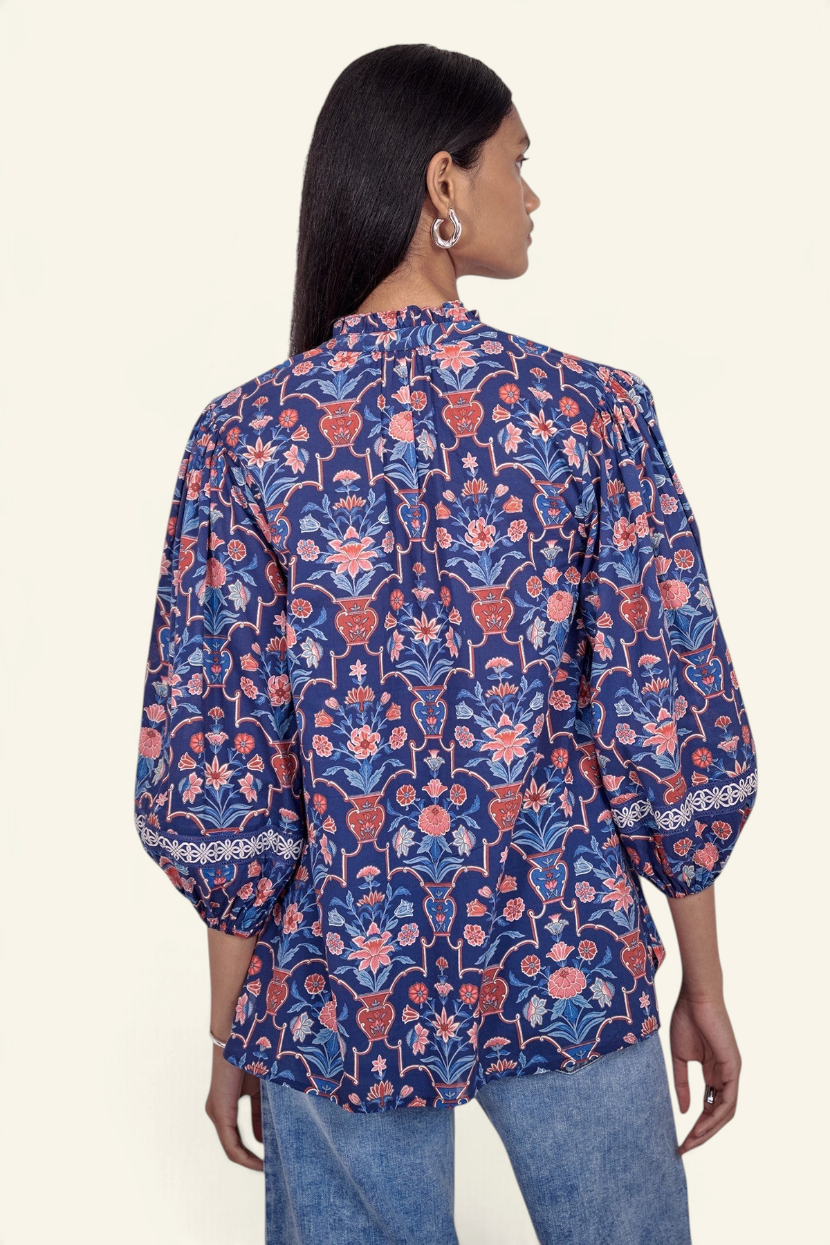 Back view of model standing wearing the Lorna top in Floral Vase print, featuring a V-neck with ruffle and tie, lace-trimmed sleeves, and a loose flowing silhouette, paired with jeans.