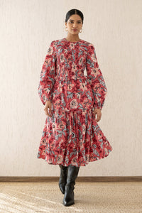 Woman stepping forward wearing the Mortiz dress with smocked detailing, ruching at the shoulders, a tiered skirt, and frilled sleeves in Elisabetta Vine Rose print.