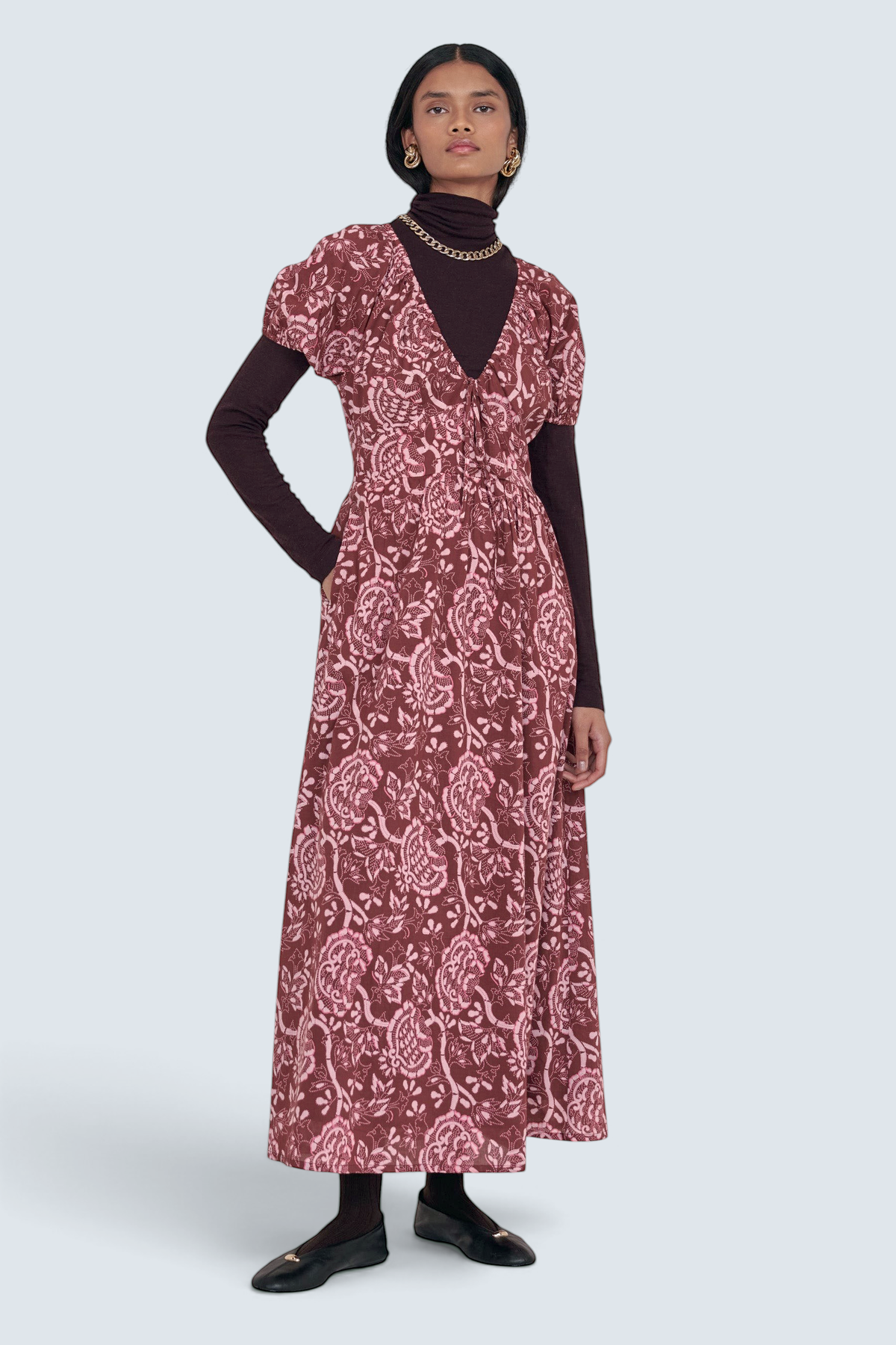 Front view of model standing. She is wearing the Norma dress in Coromandel print styled with a high neck, socks, and accessories.