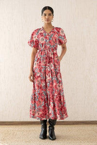 Front view of a woman wearing the Poppy dress with a hand in pocket, featuring raglan blouson sleeves, a button placket, a flowing skirt, and a drawstring waist in Elisabetta Vine Rose floral print.