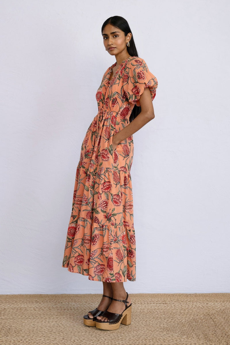 Side view of model wearing a calf length Poppy Dress in Protea Crabapple print with hands in pocket.