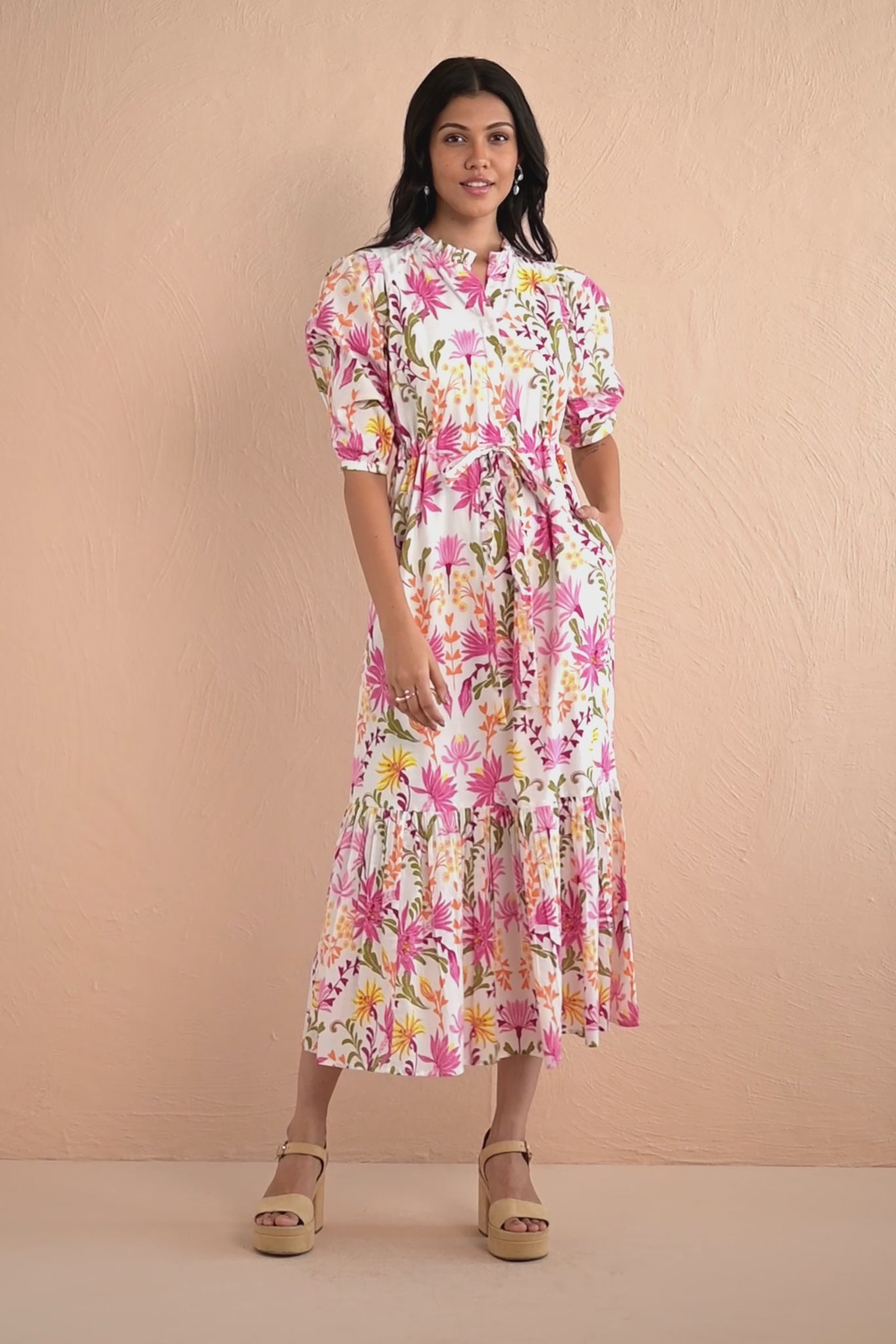 Video of woman wearing Betty Dress in Hydra Garland Rose print, featuring a cinched waist, full gathered skirt, tucked raglan sleeves, concealed front button placket, drawstring waist, and side-seam pockets in bold sunset floral cotton voile.