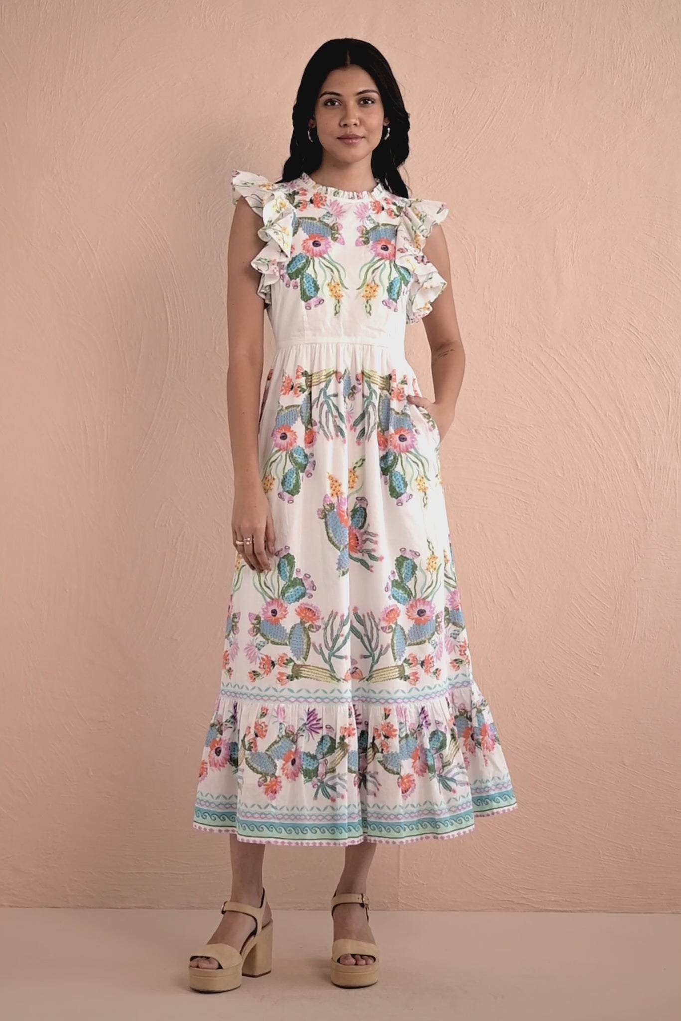 Video of a woman wearing a sleeveless white midi dress with colorful Calypso Cacti Paradise print, ruffled shoulders, a fitted waist, and a flared tiered hem.