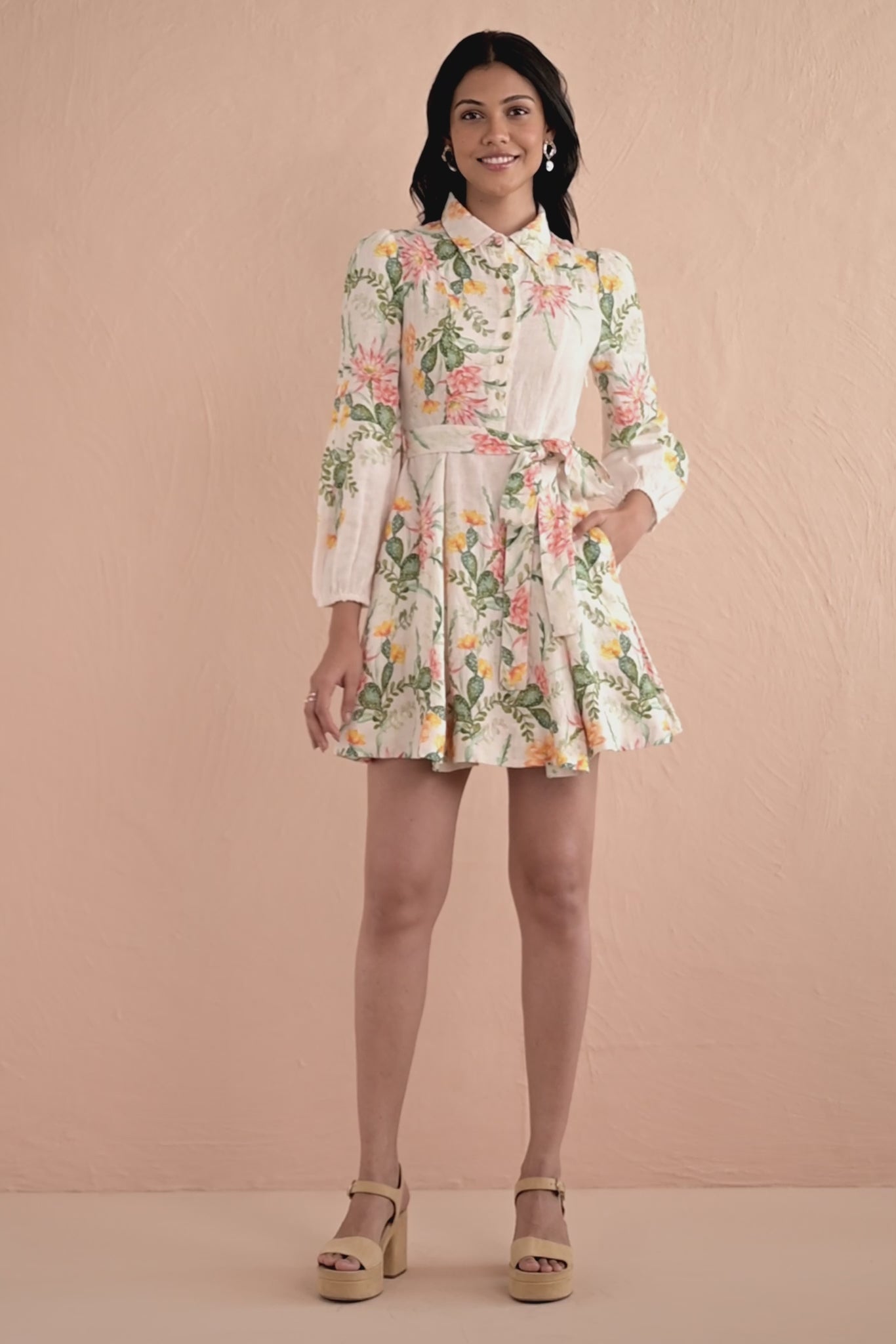 Video of woman wearing Rowena Dress in Desert Rose Dawn print, a mini linen shirtdress with delicate collar, fabric-covered buttons, elegant lantern sleeves, and side-seam pockets featuring watercolor-style cactus flowers.