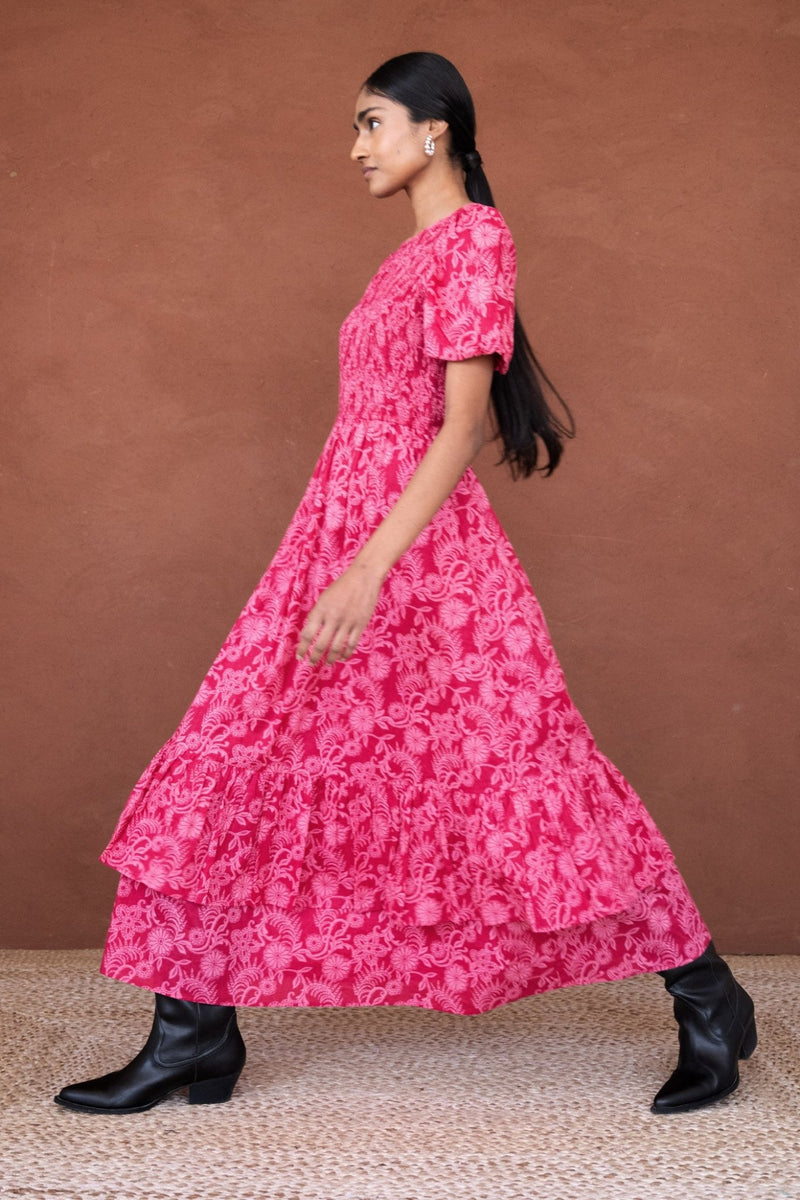 Woman walking sideways wearing the Quant midi dress in Tresse Winterberry floral print, featuring soft smocking, subtly puffed sleeves, a tiered hem, and side pockets.