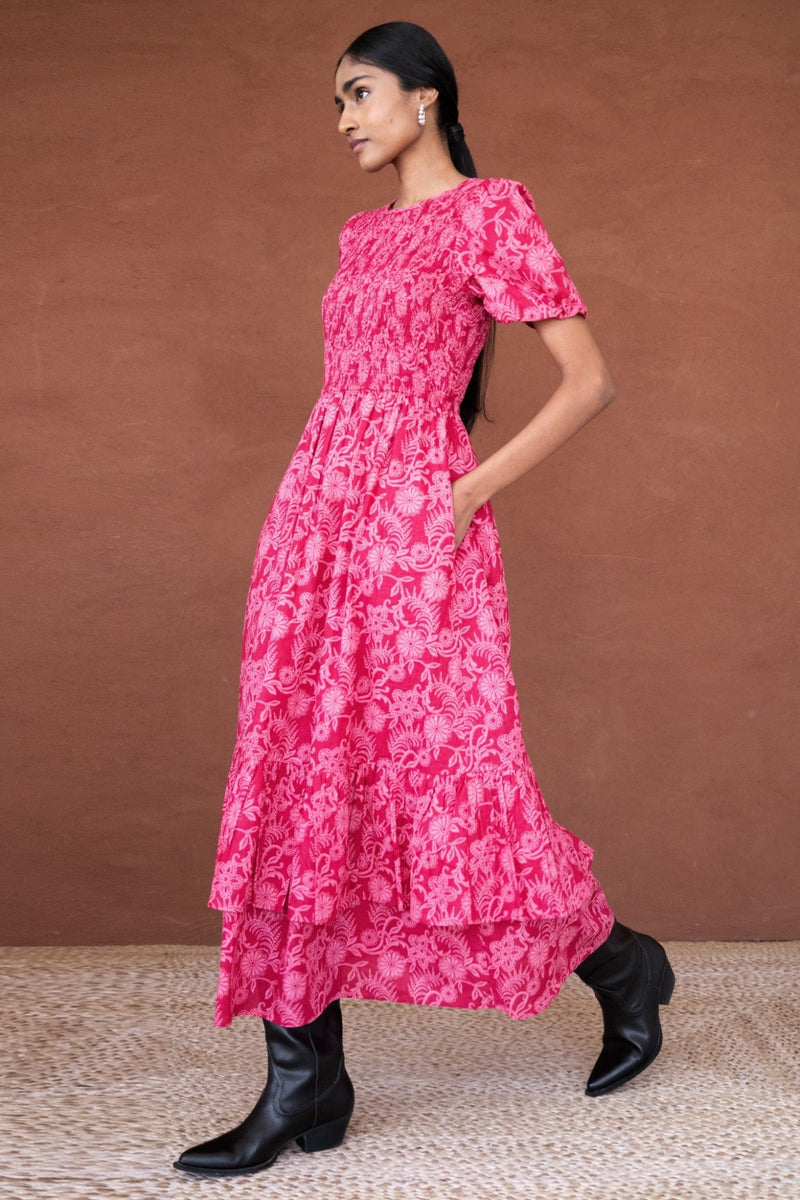 Side view of a woman wearing the Quant midi dress in Tresse Winterberry floral print, featuring soft smocking, subtly puffed sleeves, a tiered hem, and side pockets.