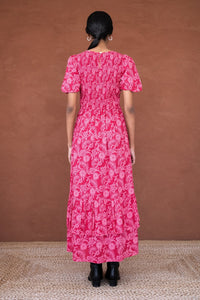 Back view of a woman wearing the Quant midi dress in Tresse Winterberry floral print, featuring soft smocking, subtly puffed sleeves, a tiered hem, and side pockets.