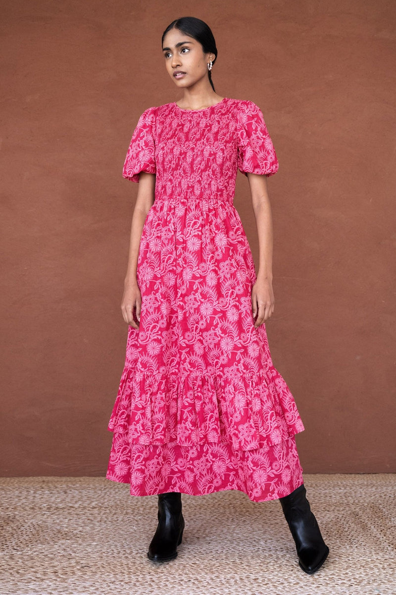 Front view of a woman wearing the Quant midi dress in Tresse Winterberry floral print, featuring soft smocking, subtly puffed sleeves, a tiered hem, and side pockets.