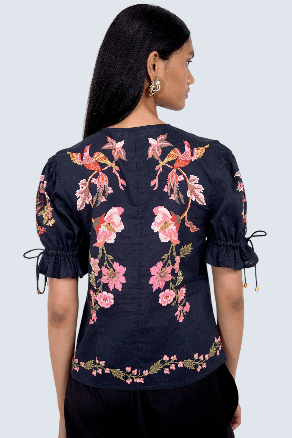 Back view of model standing. She is  wearing the Ricki top in Chintz print, featuring a adjustable drawstring sleeves, and vintage-inspired print placement. Its paired with black pants.