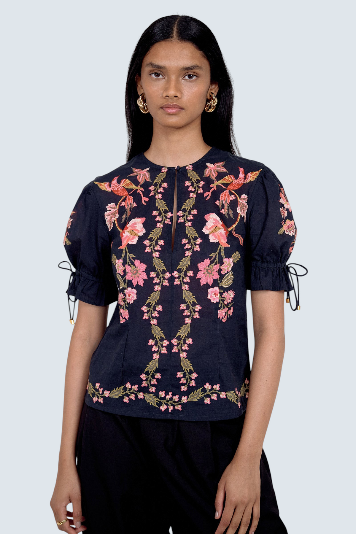 Front view of model standing. She is  wearing the Ricki top in Chintz print, featuring a crewneck with keyhole detail, adjustable drawstring sleeves, and vintage-inspired print placement. Its paired with black pants.