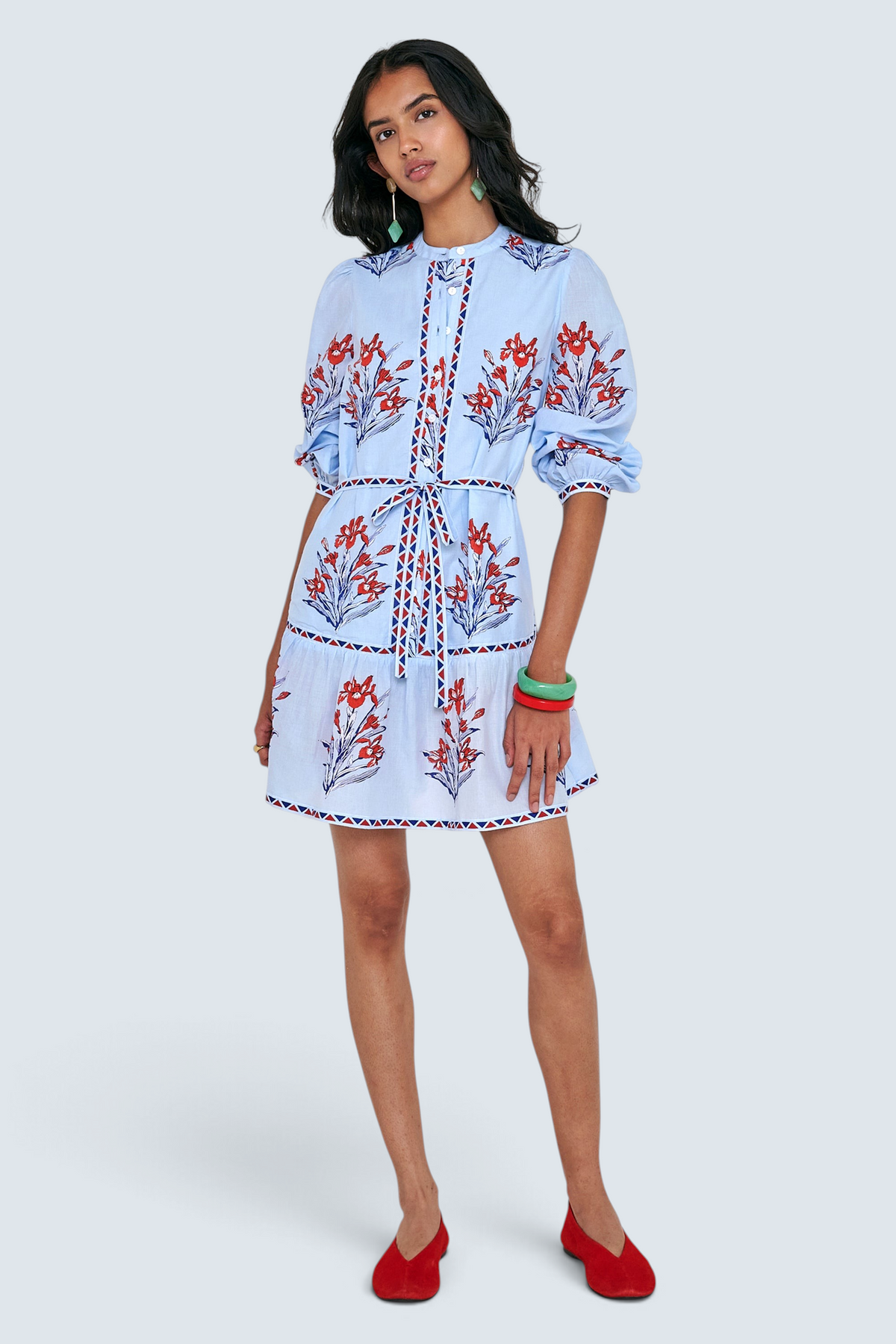 Front view of woman standing. She is wearing the Roma dress in the Brigitte print, featuring a mini shirtdress silhouette, contrast trim details, a detachable belt, and blooming iris floral motifs.