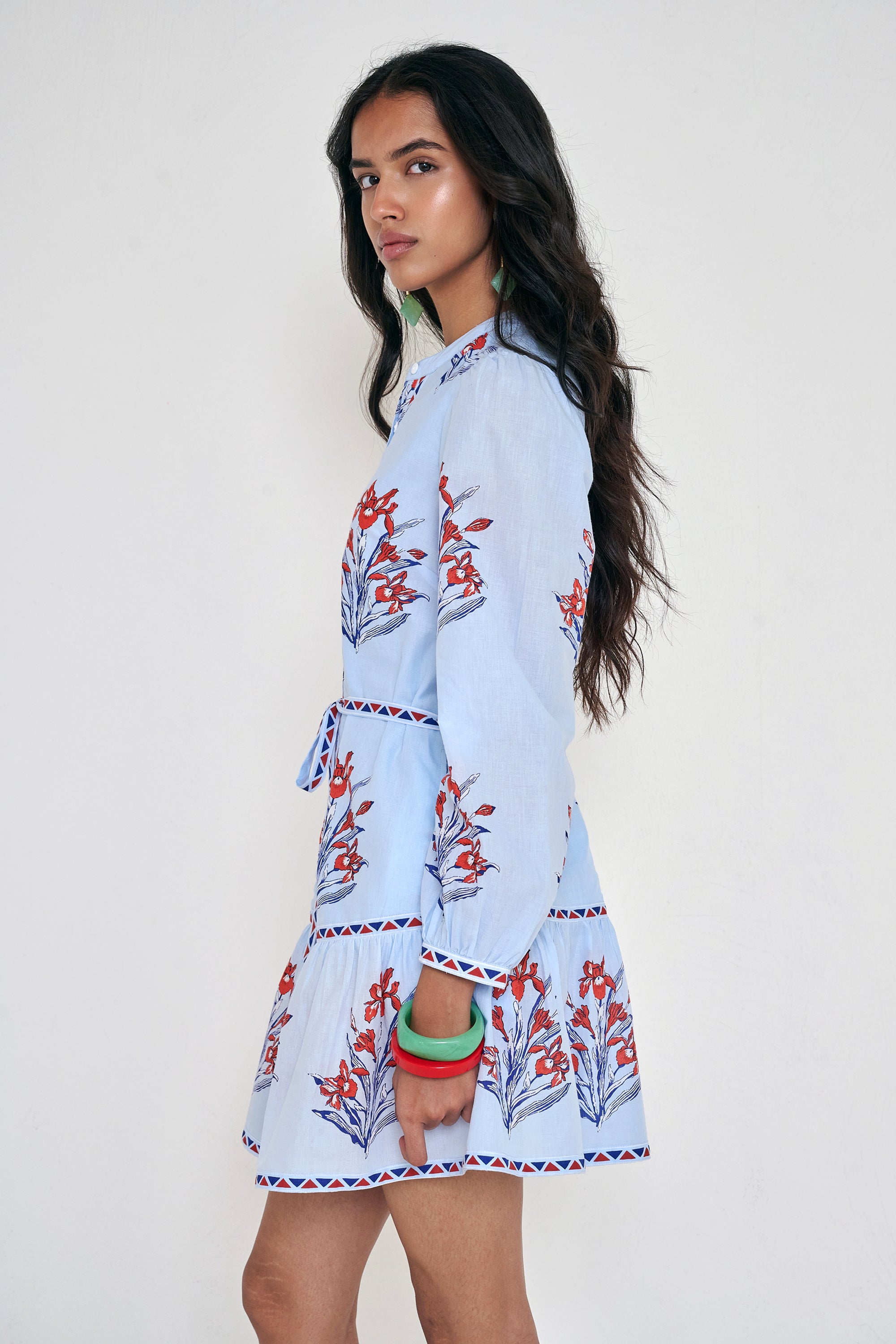 Side view of woman standing. She is wearing the Roma dress in the Brigitte print, featuring a mini shirtdress silhouette, contrast trim details, a detachable belt, and blooming iris floral motifs.