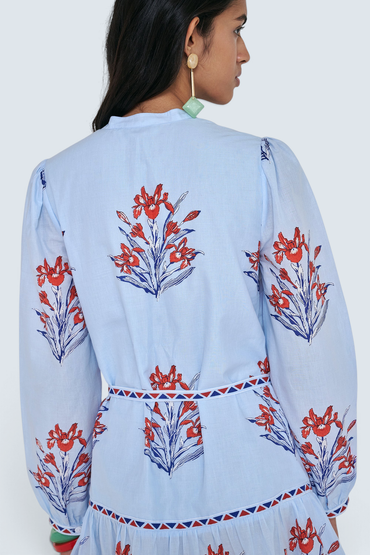 Back view close up of woman standing. She is wearing the Roma dress in the Brigitte print, featuring a mini shirtdress silhouette, contrast trim details, a detachable belt, and blooming iris floral motifs.