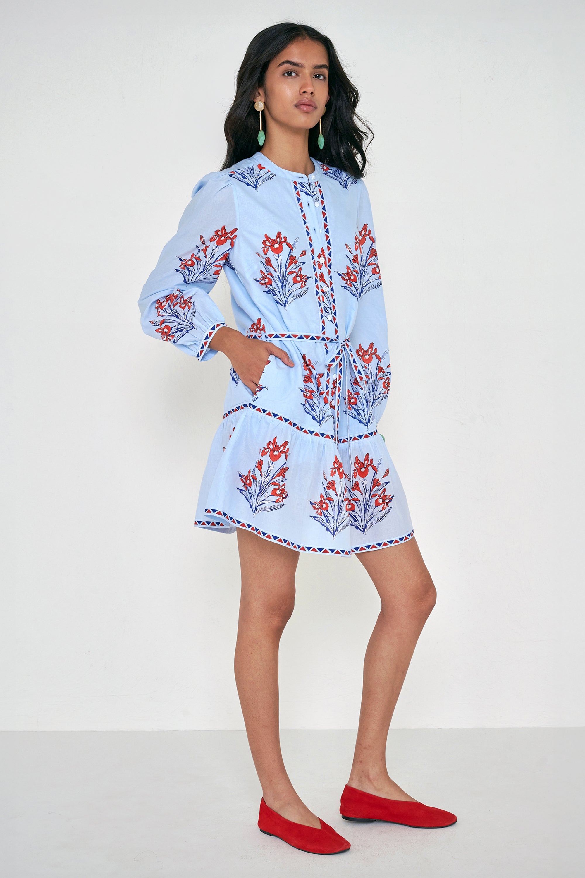Side view of woman standing. She is wearing the Roma dress in the Brigitte print, featuring a mini shirtdress silhouette, contrast trim details, a detachable belt, and blooming iris floral motifs.