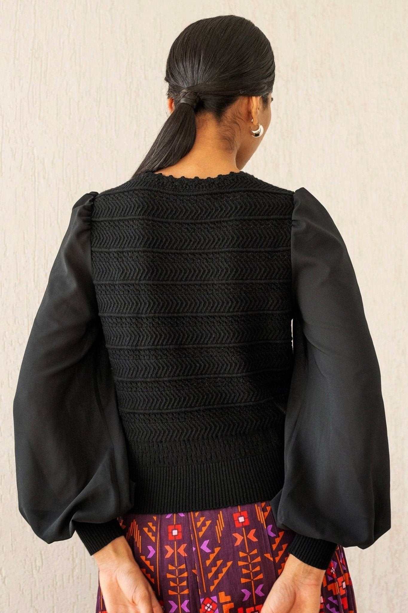 Back view of woman wearing the Rosie knit, featuring hand-crocheted details and viscose georgette sleeves, blending structure with textural complexity.