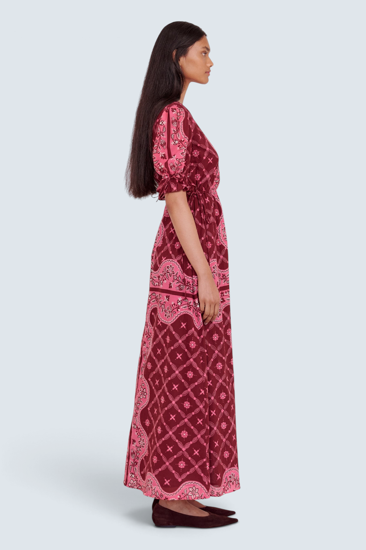 Side view of model standing. She is wearing the Ruby dress in Bandana print, featuring a keyhole neckline, adjustable drawstring waist and sleeves, and side-seam pockets.