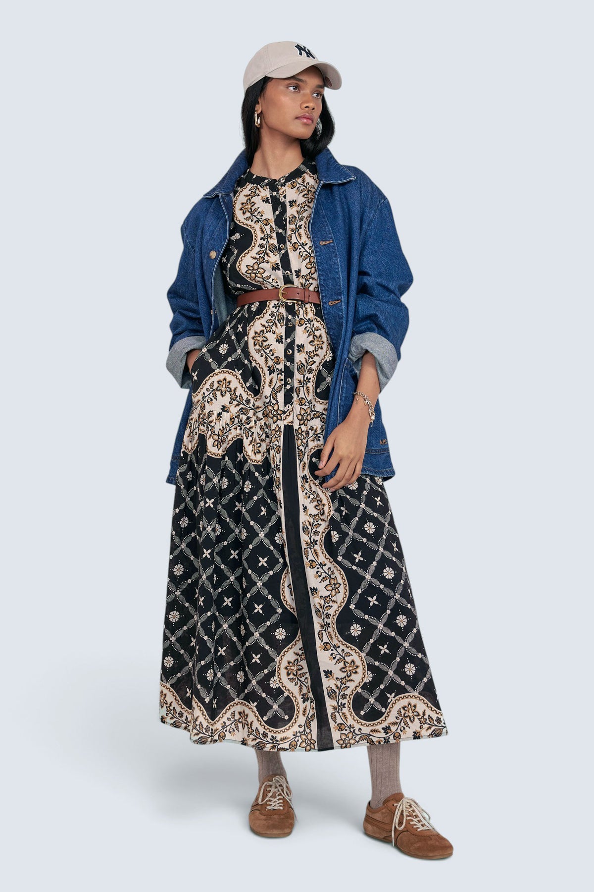 Front view of model standing. She is wearing the Saylor dress in Bandana print, featuring a full-length shirtdress silhouette with tiered skirt. Its paired with denim oversized shirt, NY cap, brown belt, socks and shoe.