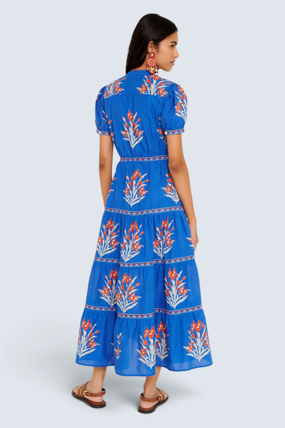 Back view of woman standing. She is  wearing the Saylor dress in the Brigitte print, featuring a full-length shirtdress silhouette, tiered skirt, detachable belt, and hand-screen-printed iris floral motifs.