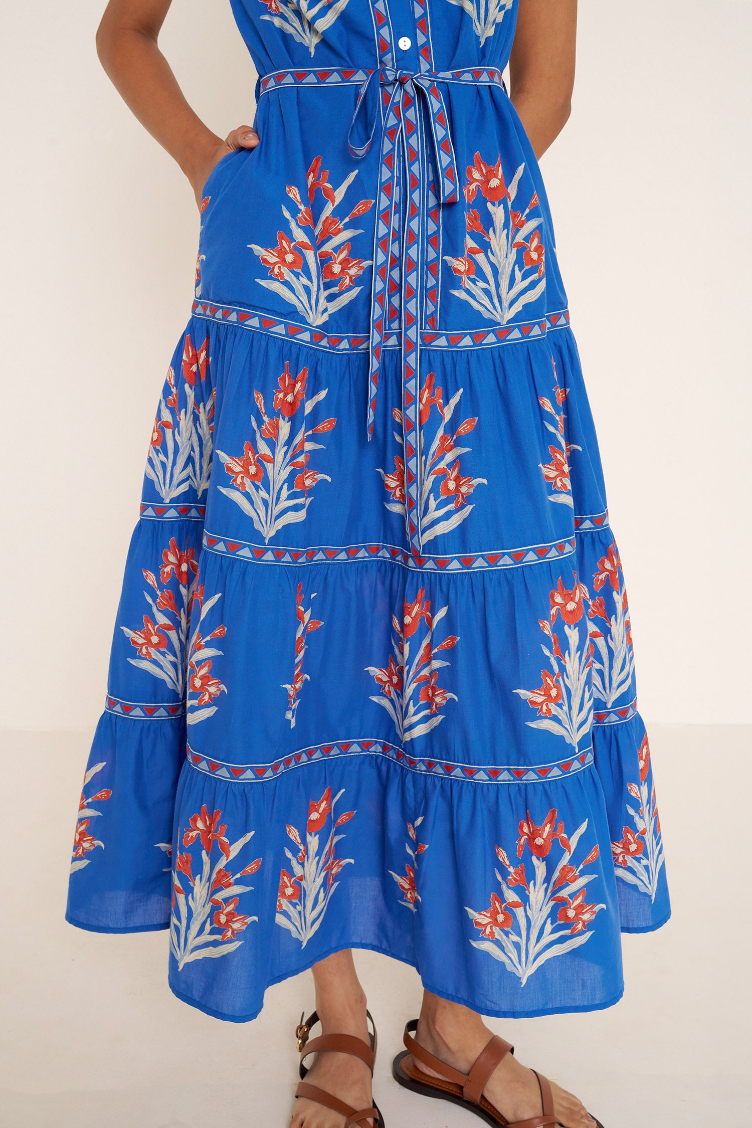 Front view close up of woman standing. She is  wearing the Saylor dress in the Brigitte print, featuring a full-length shirtdress silhouette, tiered skirt, detachable belt, and hand-screen-printed iris floral motifs.
