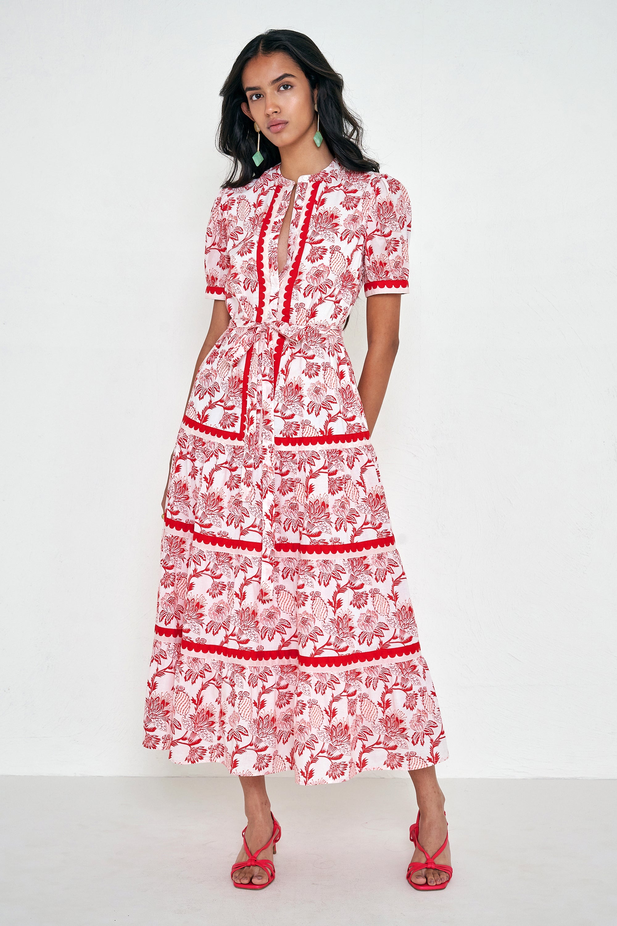 Front view of woman standing. She is  wearing the Saylor dress in the Lizzie floral print, featuring a full-length shirtdress silhouette, tiered skirt, detachable belt, and winding floral vine motifs.