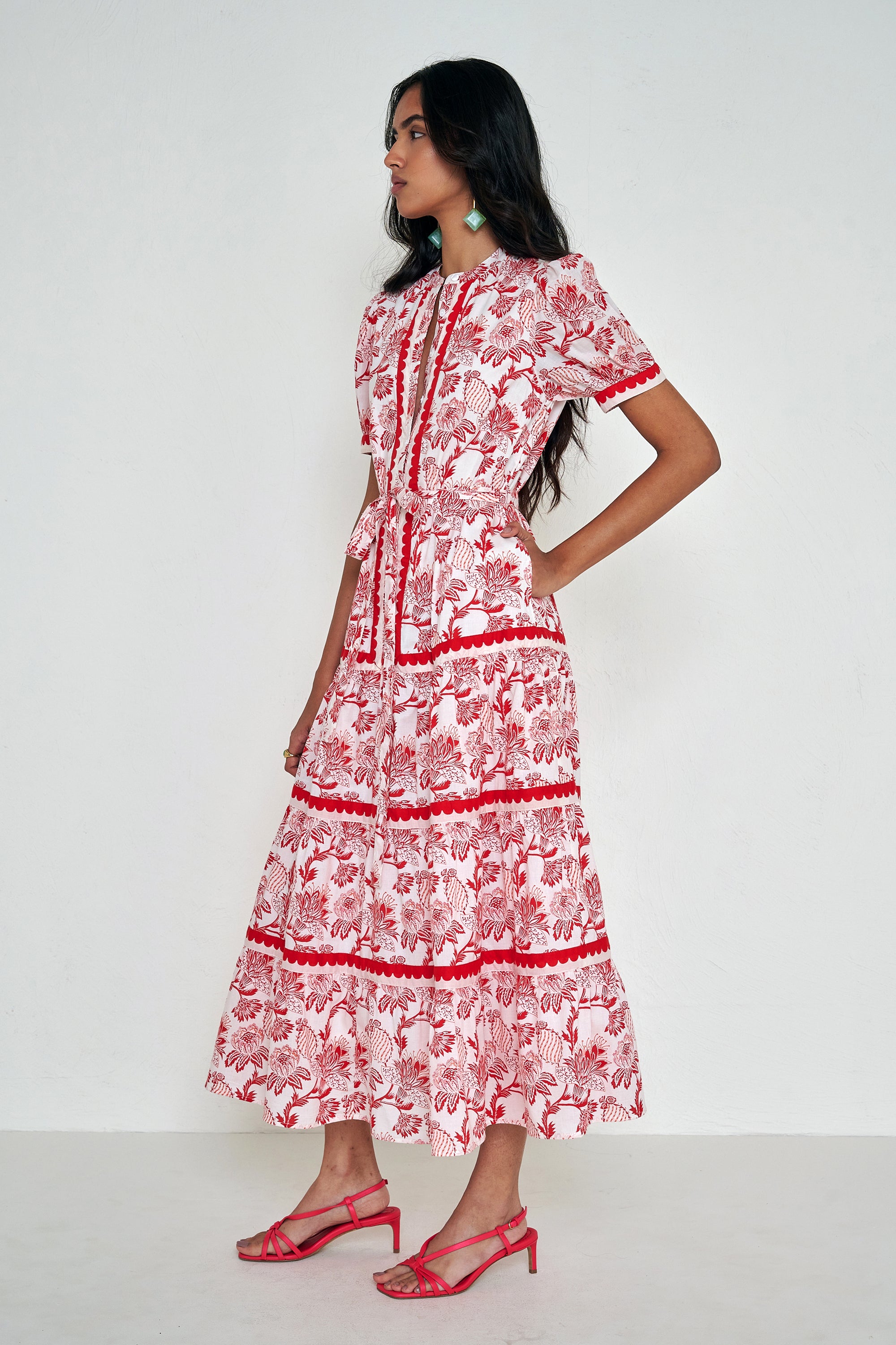 Side view of woman standing. She is  wearing the Saylor dress in the Lizzie floral print, featuring a full-length shirtdress silhouette, tiered skirt, detachable belt, and winding floral vine motifs.