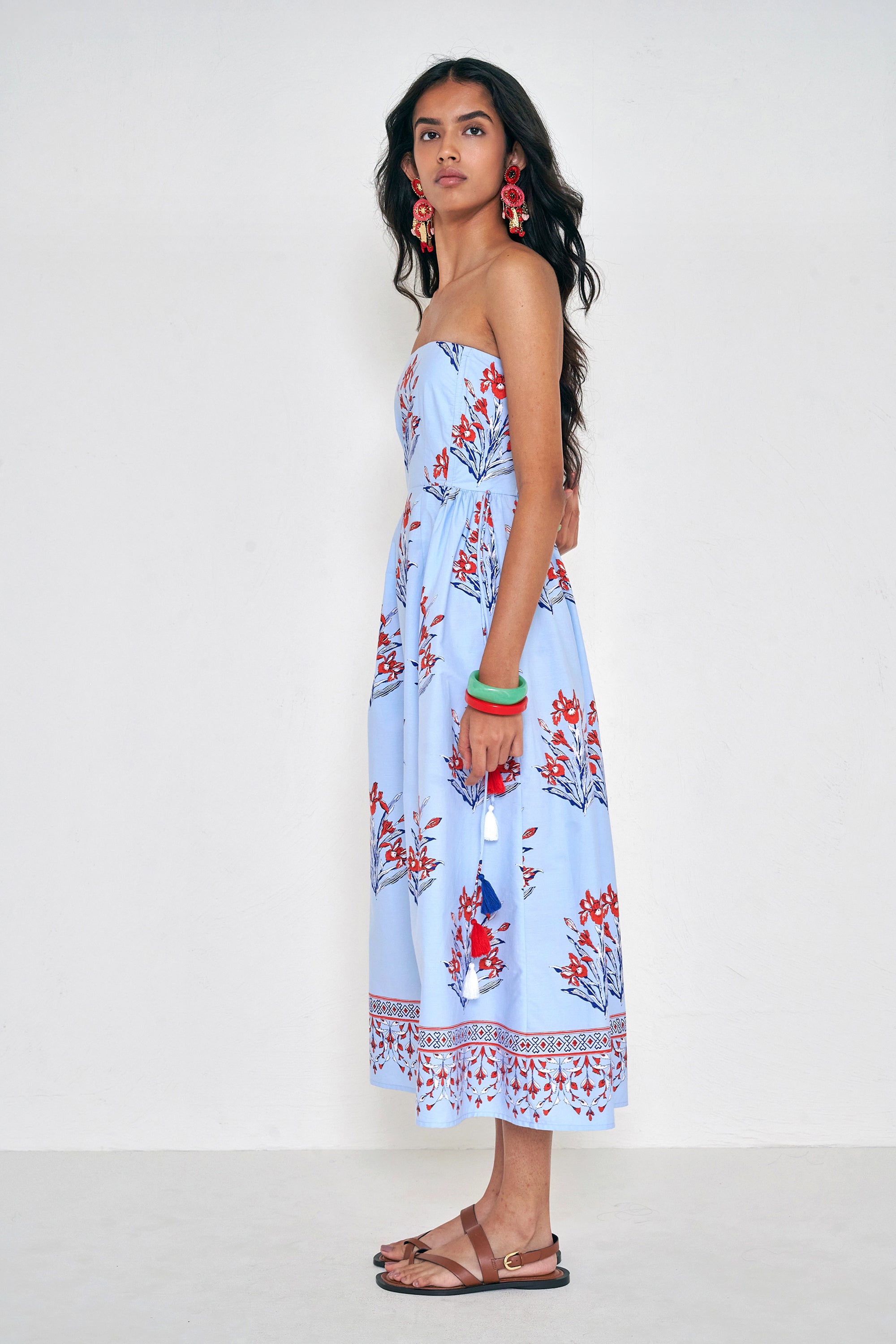 Side view of woman standing. She is  wearing the Simona dress in the Brigitte floral print, featuring a strapless bodice, full gathered skirt, and red, white, and blue iris motifs.