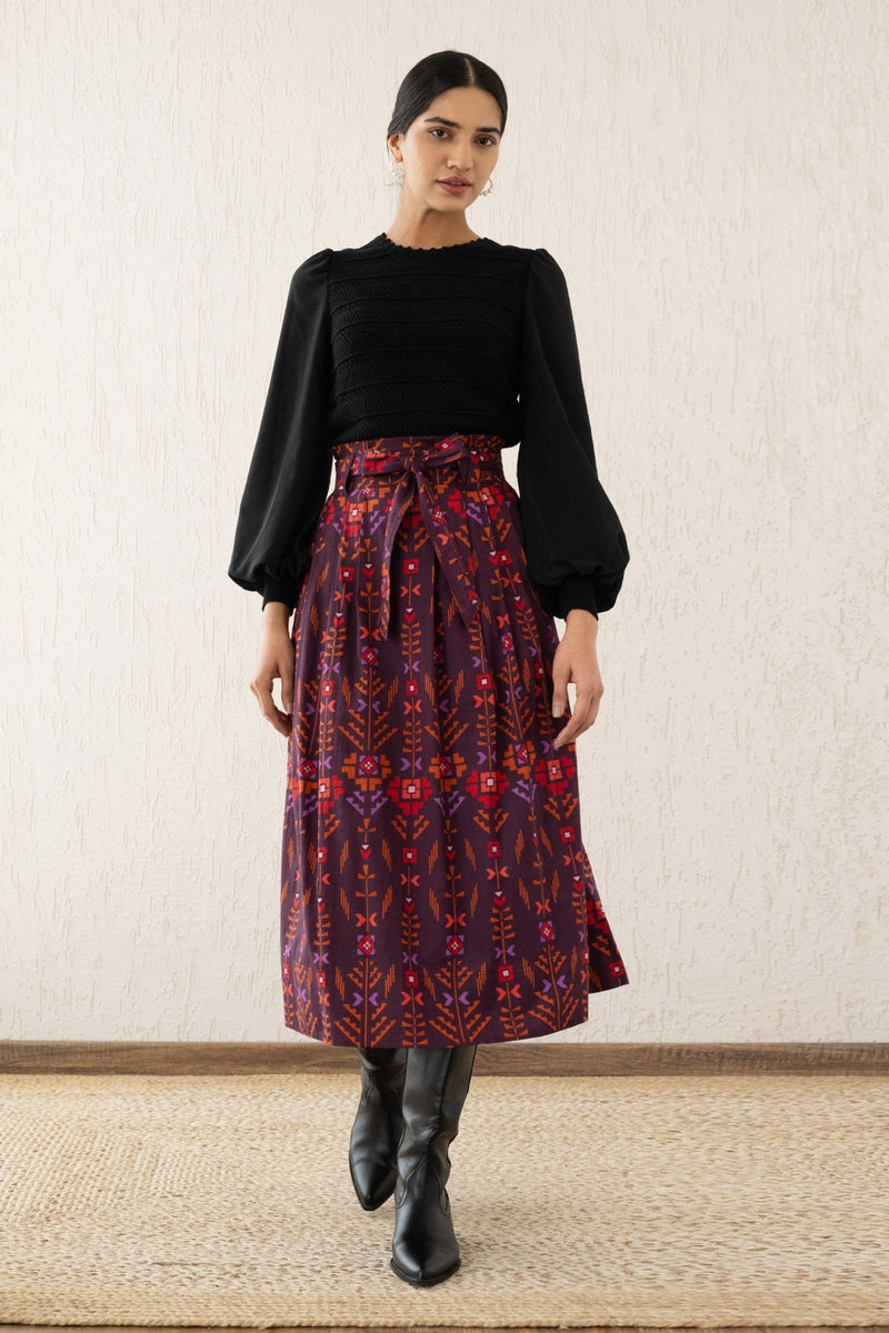 Woman stepping forward wearing the Tobias skirt with a paper bag waist, self-tie belt, and pockets in Emilie Deco Cinnamon print, inspired by Austrian Art Nouveau.