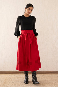 Front view of a woman wearing the Tobias skirt in Tango with a paper bag waist, self-tie belt, and pockets, featuring Art Nouveau-inspired roses in the Lace embroidery.