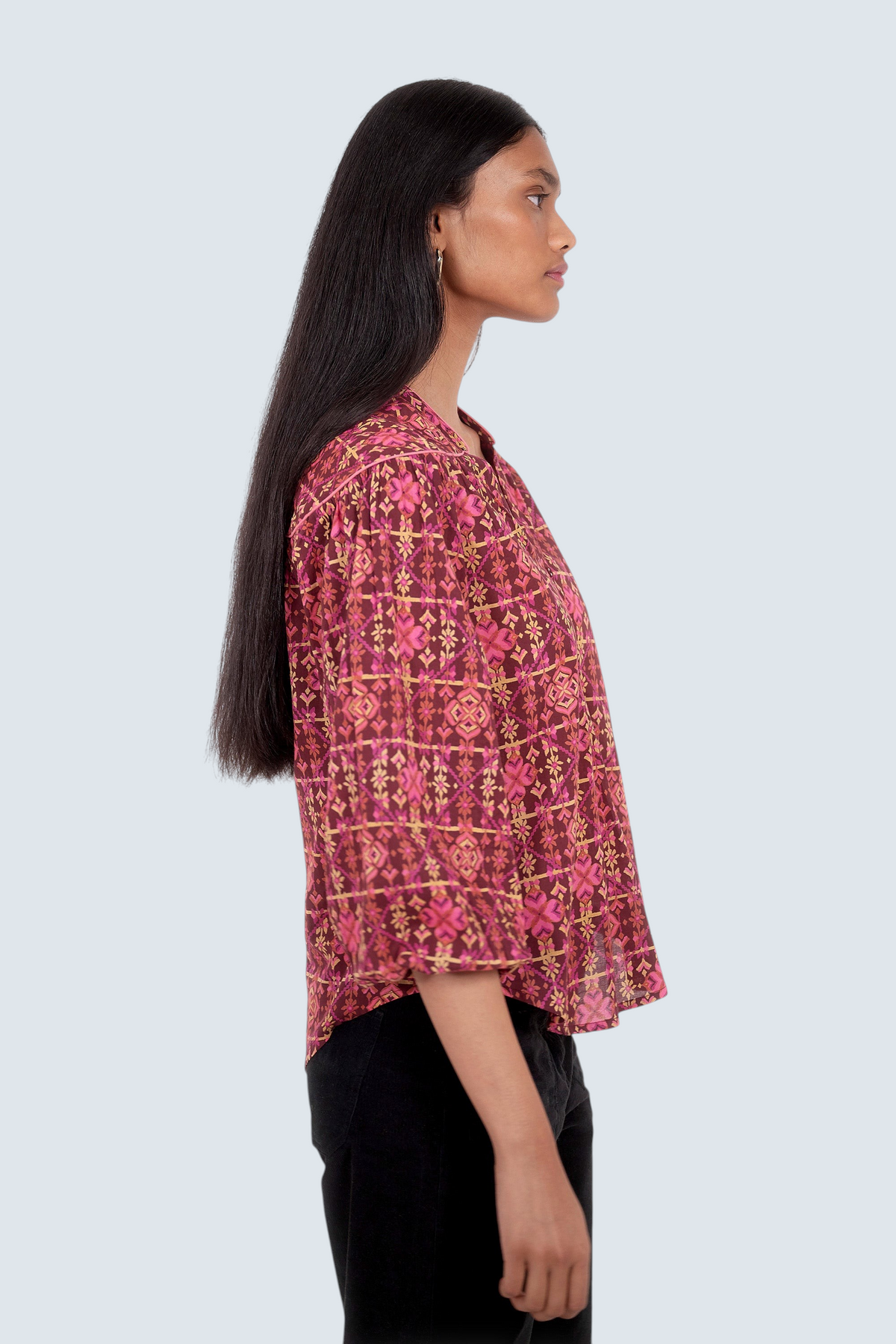 Side view of model standing. She is wearing Banjanan Vanessa top in mahogany cotton voile with a pink geometric floral needlepoint print and v-neckline.
