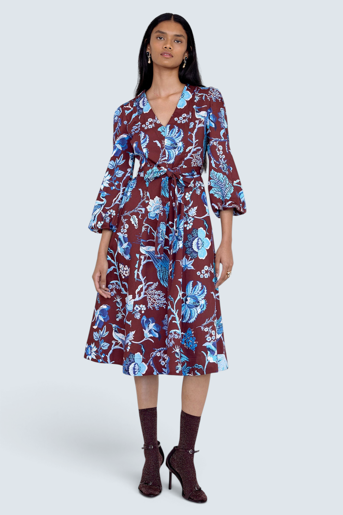 Front view of model standing. She is  wearing the Zora dress in Chintz print, featuring a V-neck, lantern sleeves, princess seams, a gathered fit-and-flare skirt, fabric belt, and side-seam pockets.